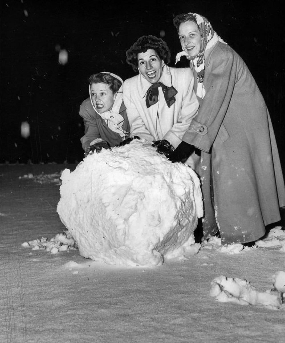 Women rolling a giant snowball in a front yard in Bel-Air.