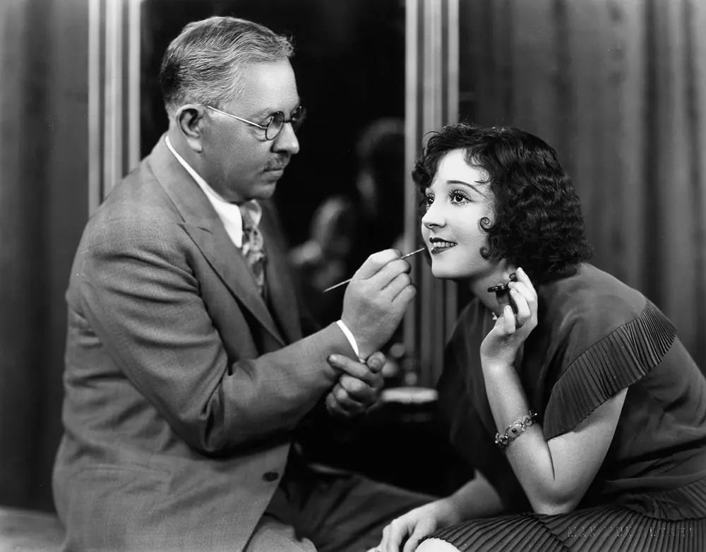 Factor applies lipstick to silent film star Madge Bellamy. 1930.