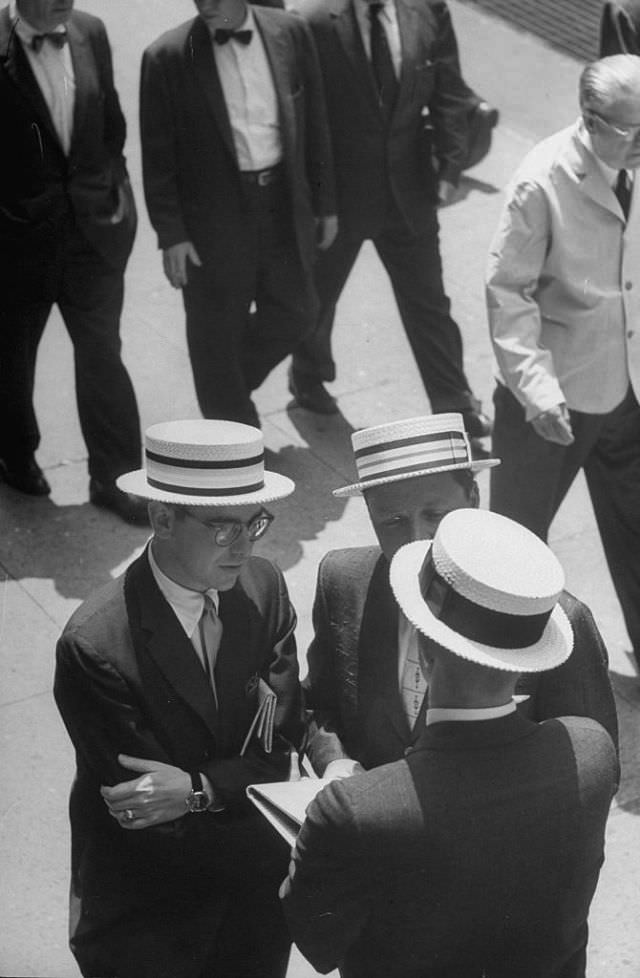 Elevated view of a trio of men in suits and straw boaters as they talk on a sidewalk, New York, 1958.