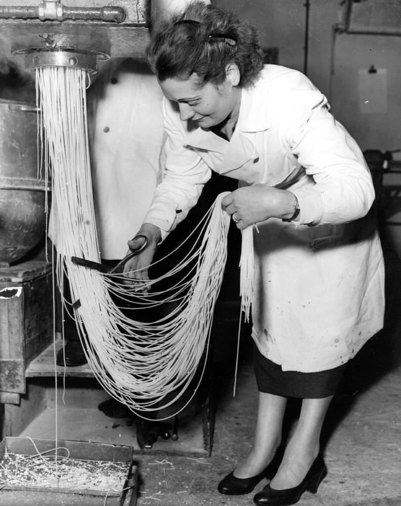 Zelda Albano cuts spaghetti into lengths as it emerges from a machine at Mess' L Ugo Ltd, a pasta making factory in Holloway, London, 1955