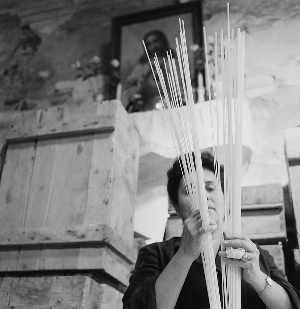 A woman holding strands of pasta, Italy, 1955.
