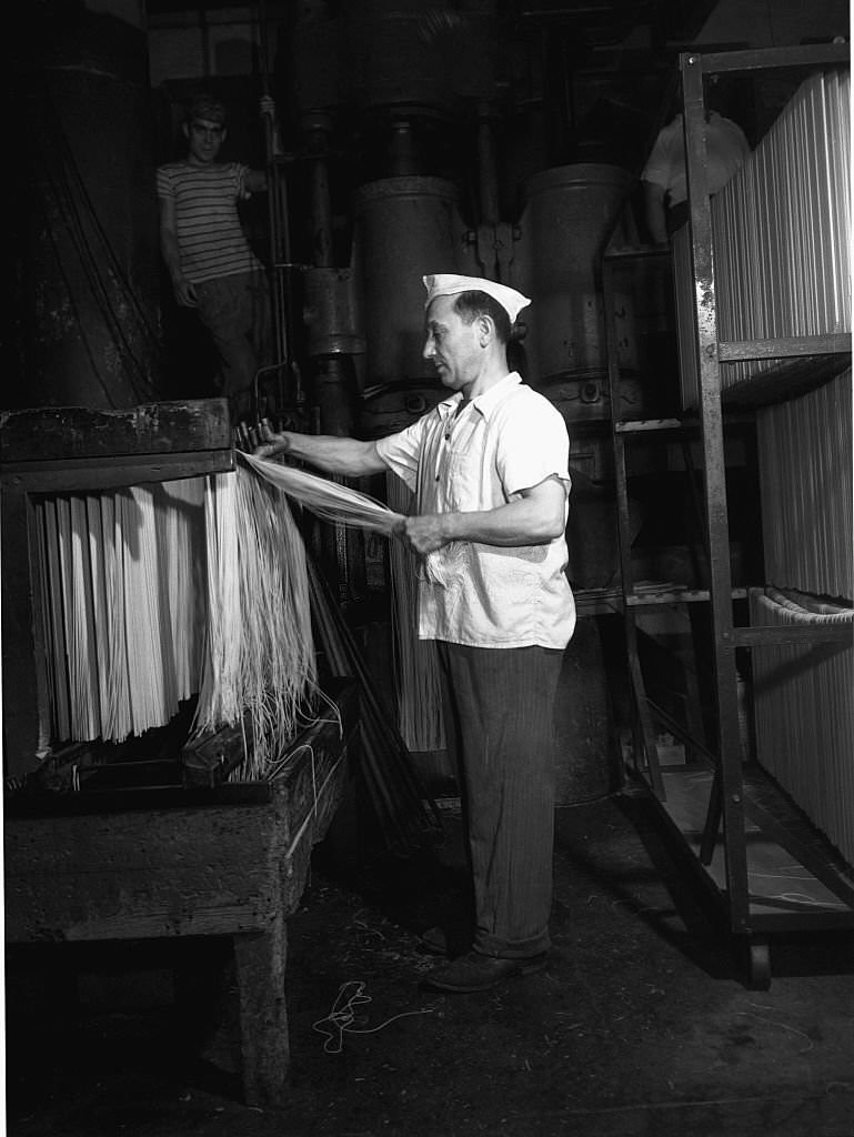 A worker for Atlantic Macaroni Company, makers of Caruso brand products, hanging spaghetti to dry, 1943
