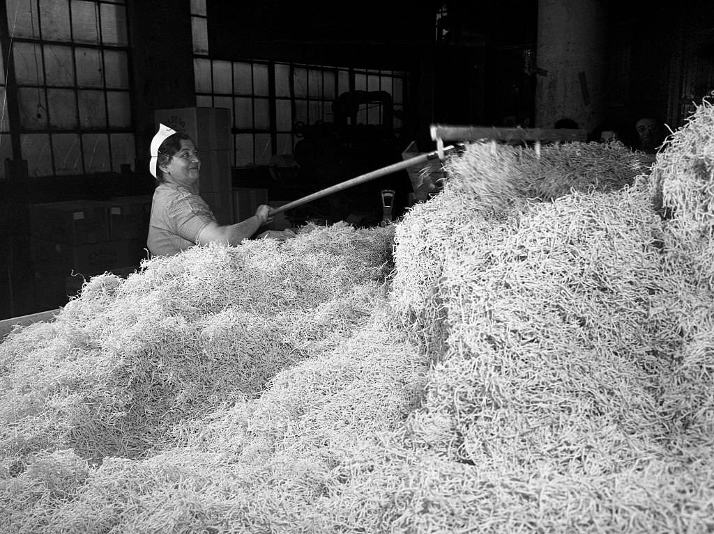 A worker at the Atlantic Macaroni Company, makers of Caruso brand products, keeping the chute clear of finished macaroni in Long Island City, New York, 1943