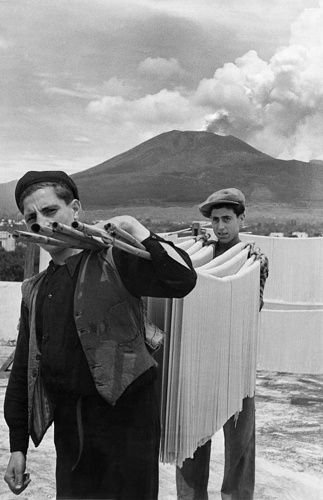 Spaghetti production Two men carrying spaghetti on a bamboo stick to dry them, 1932