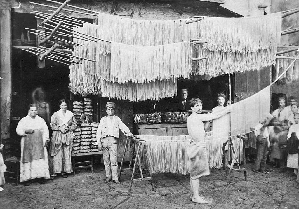 Macaroni being hung to dry so that it may be sold in the market where the people are standing.