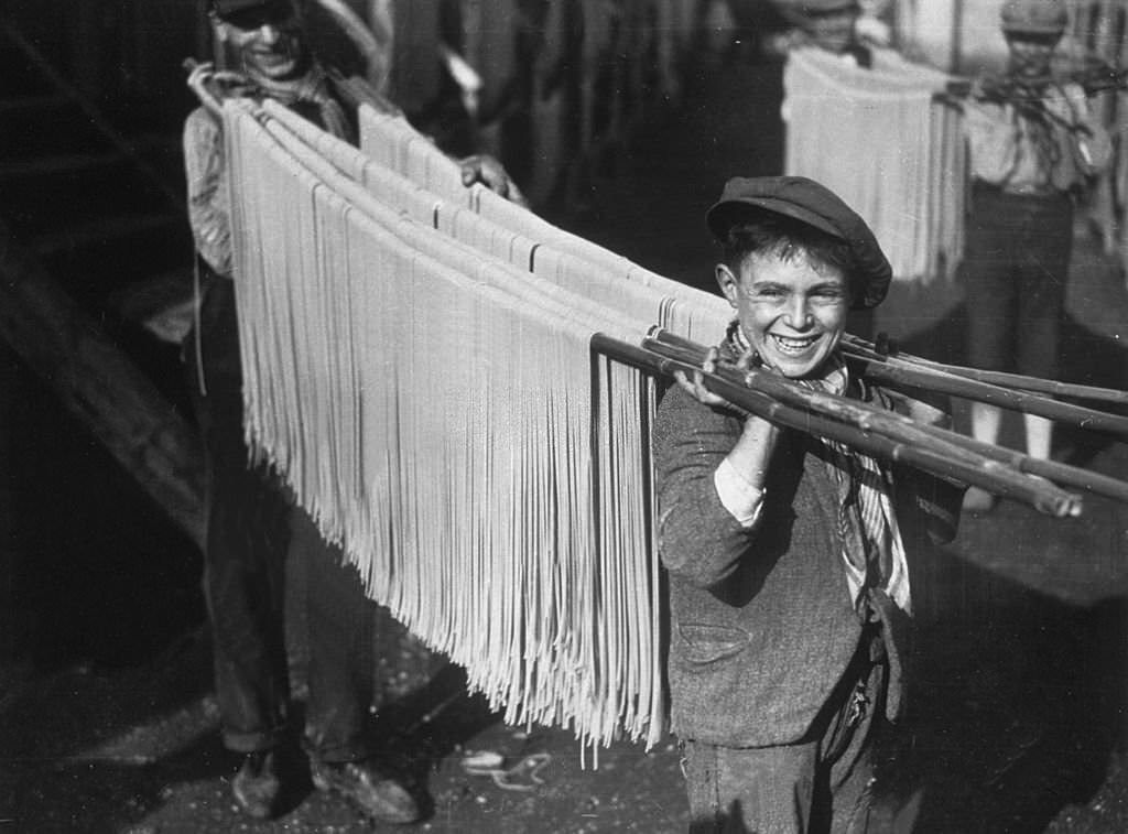 A young boy carrying strings of pasta in a macaroni factory in Naples, Italy. 1929