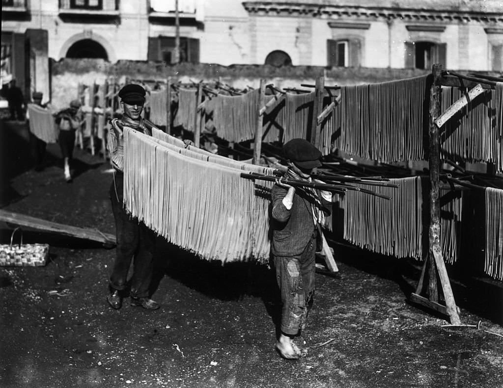 Boys carrying racks of spaghetti to be hung out to dry