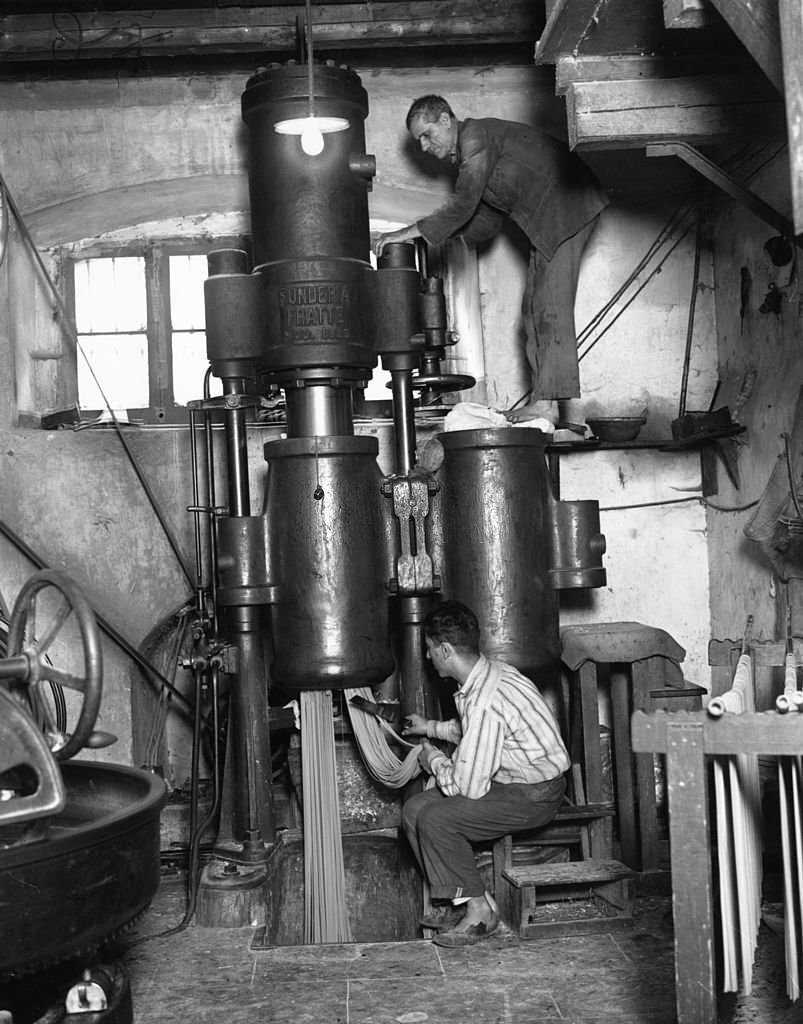 Two men operating a pasta making machine, the man at the bottom cutting off lengths of pasta, in Naples.