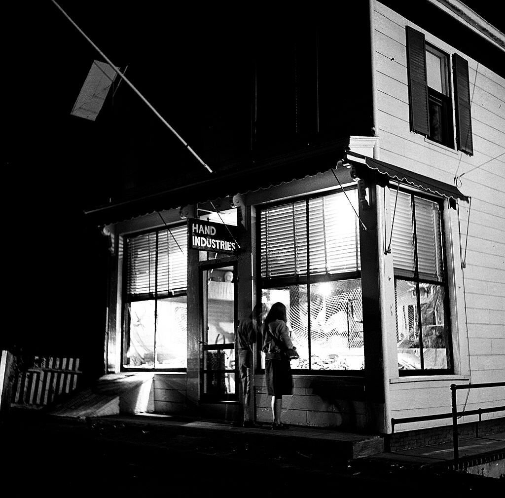 Night time view as two visitors look intot the window of the Hand Industries shop, Provincetown, Massachusetts, 1948.