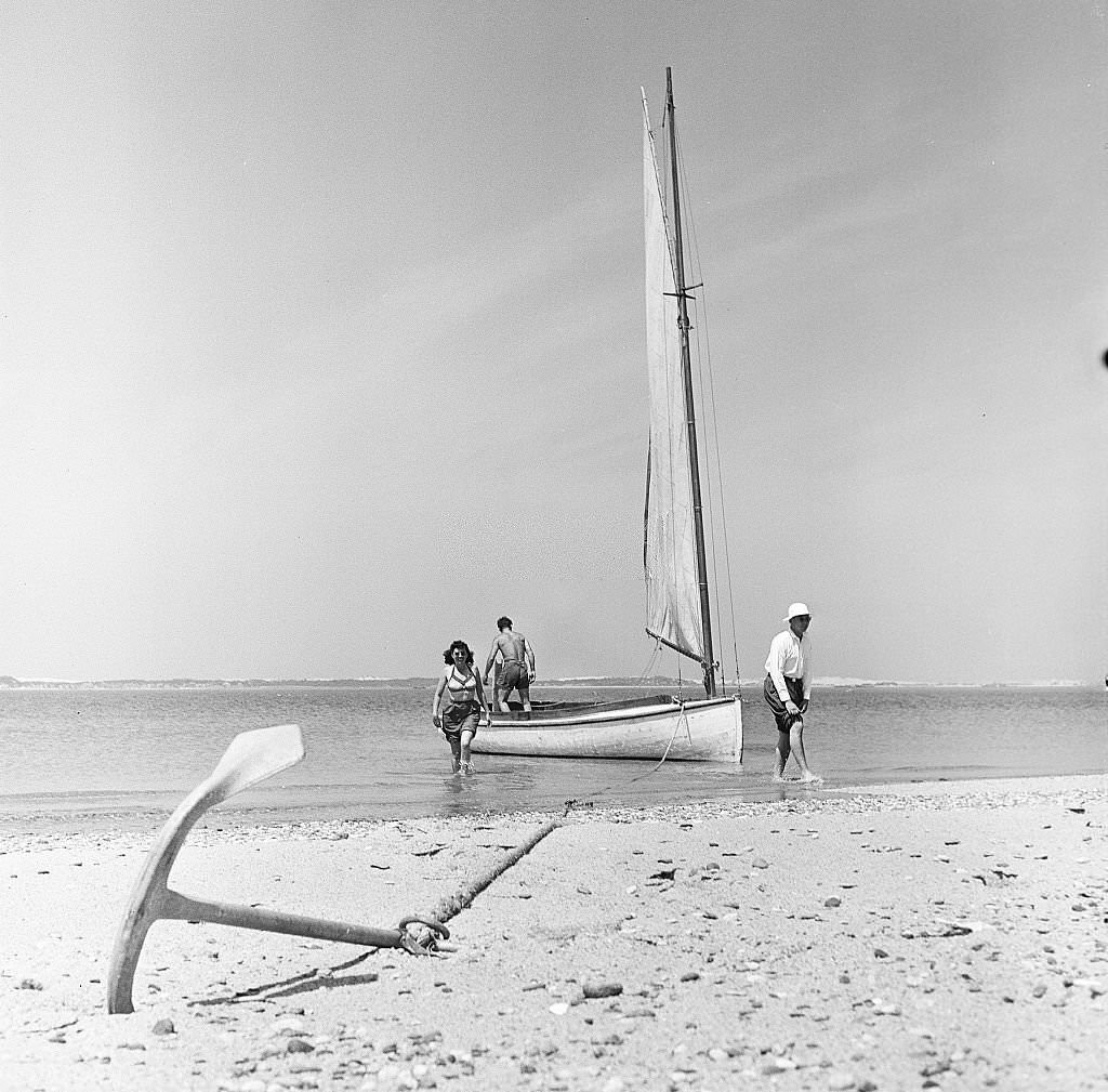 A sailboat sits at anchor on the beach as two men and a woman start to debark on Cape Cod, Provincetown, Massachussetts, 1947.