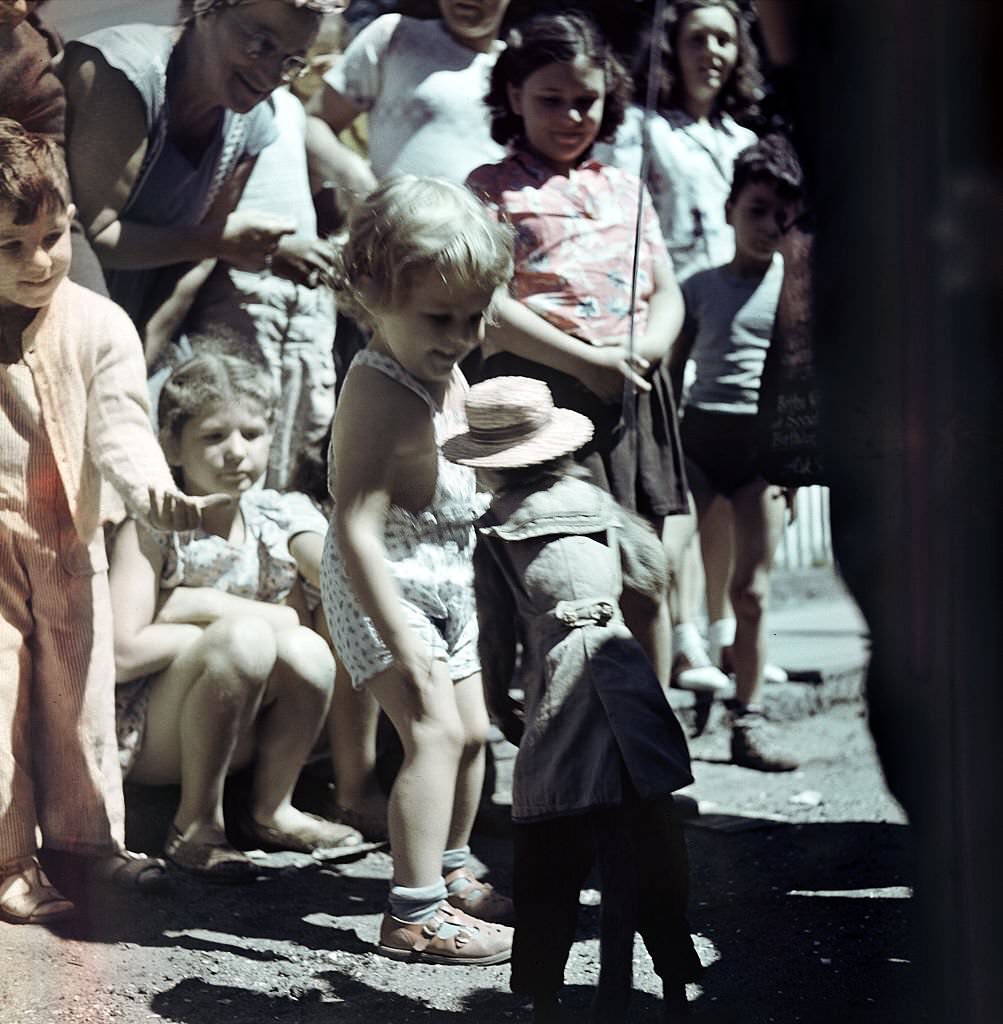 A young child plays with a monkey as other children gather around, Provincetown, Massachusetts, 1948.