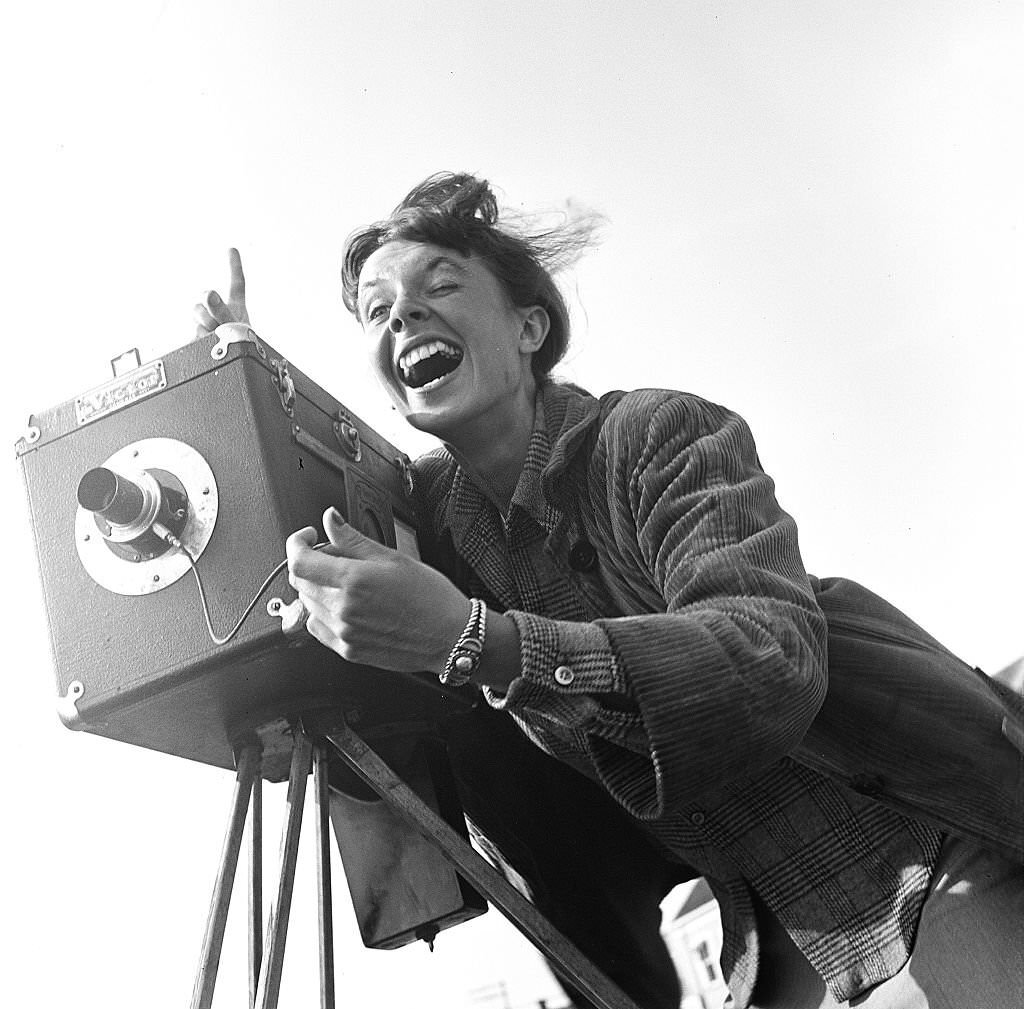 A photographer smiles while taking photographs using a tripod camera and a handheld shutter release, Provincetown, Massachusetts, 1948.