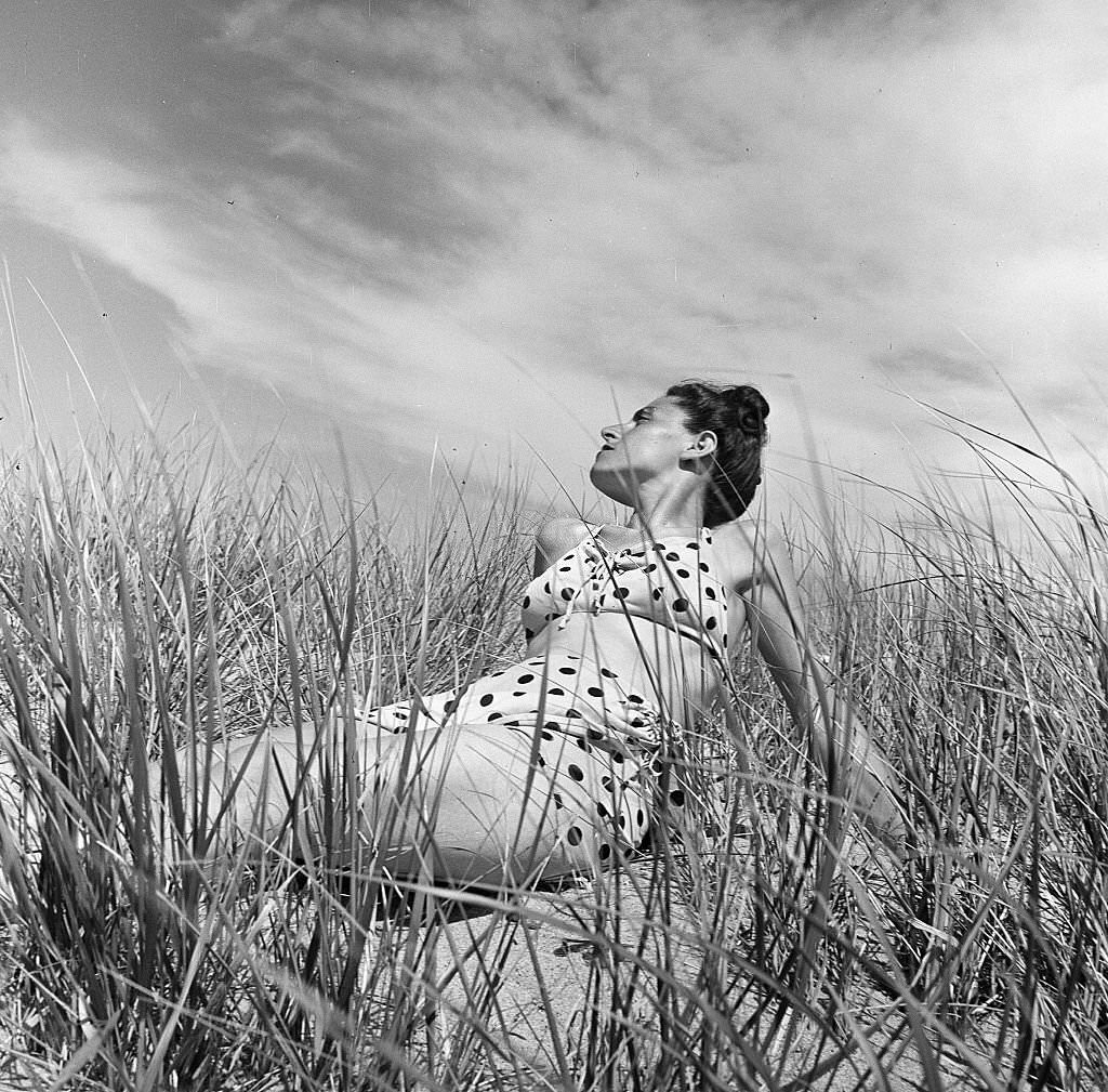 Portrait of a woman wearing a polka dot bathing suit and seated among the plants on the beach, Provincetown, Massachusetts, 1948.