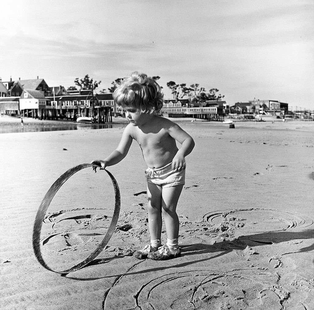 A young child plays with a hoop on the beach, Provincetown, Massachusetts, 1948.