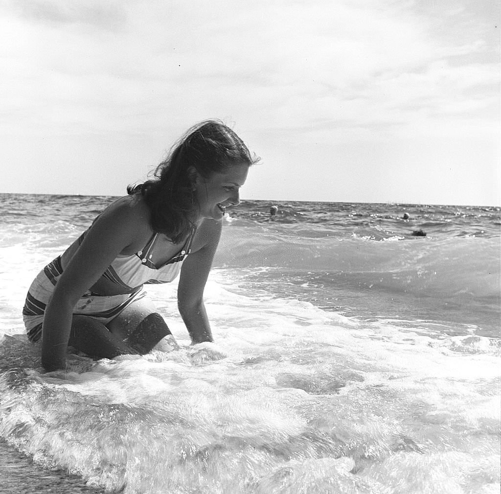 A woman smiles while sitting on the beach as the surf rolls, Provincetown, Massachusetts, 1948.