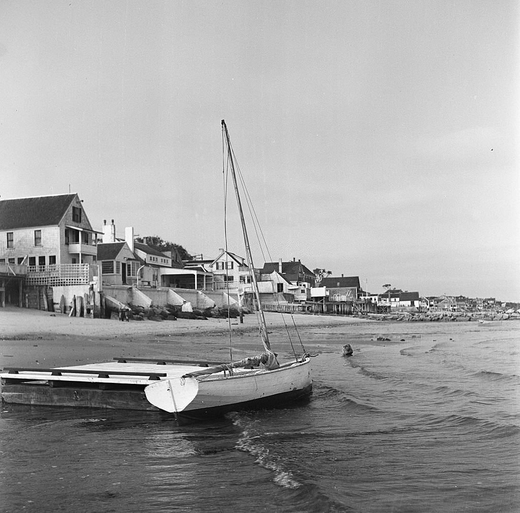 View of a small sailboat docked to a beached raft with beachside houses in the distance, Provincetown, Massachusetts, 1948.