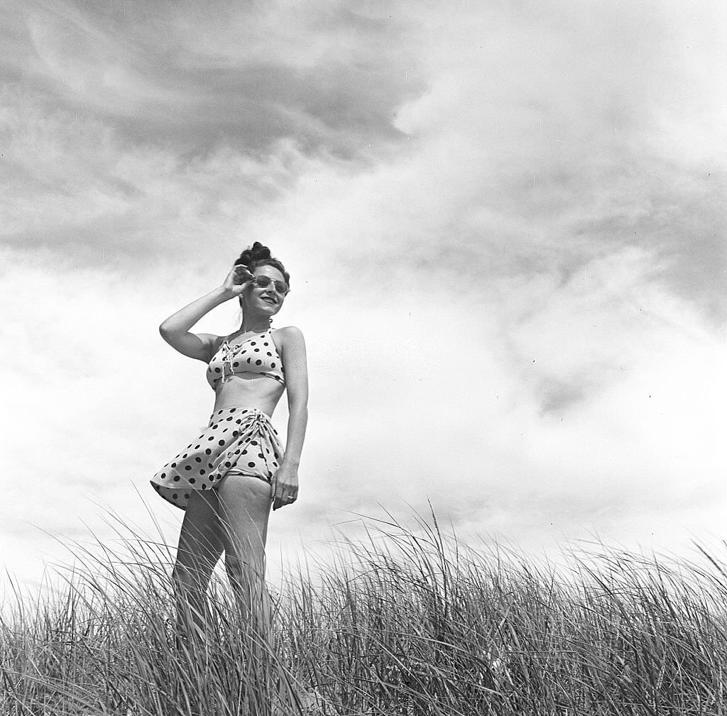A woman wearing a polka dot bathing suit and standing among the plants on the beach, Provincetown, Massachusetts, 1948.