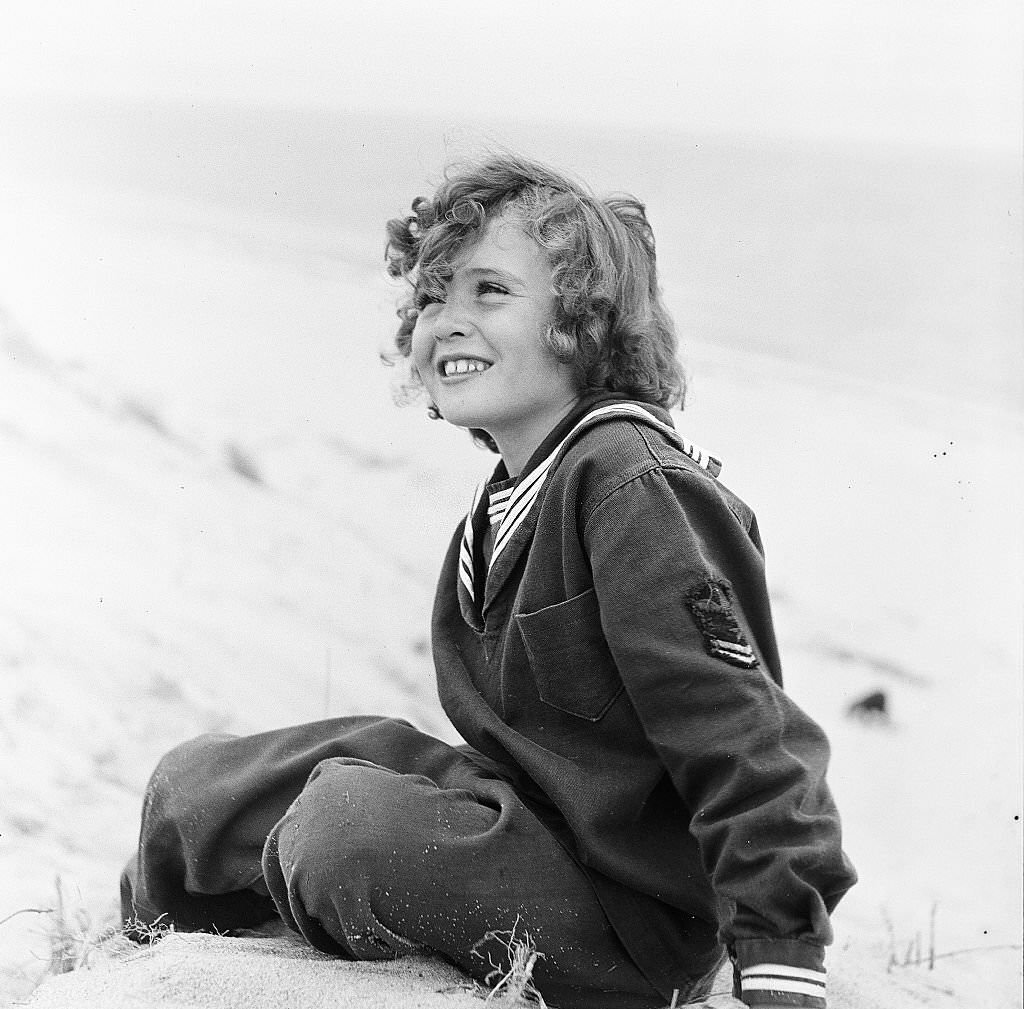 Young girl smiles while sitting on the beach on Cape Cod, Provincetown, Massachussetts, 1947.
