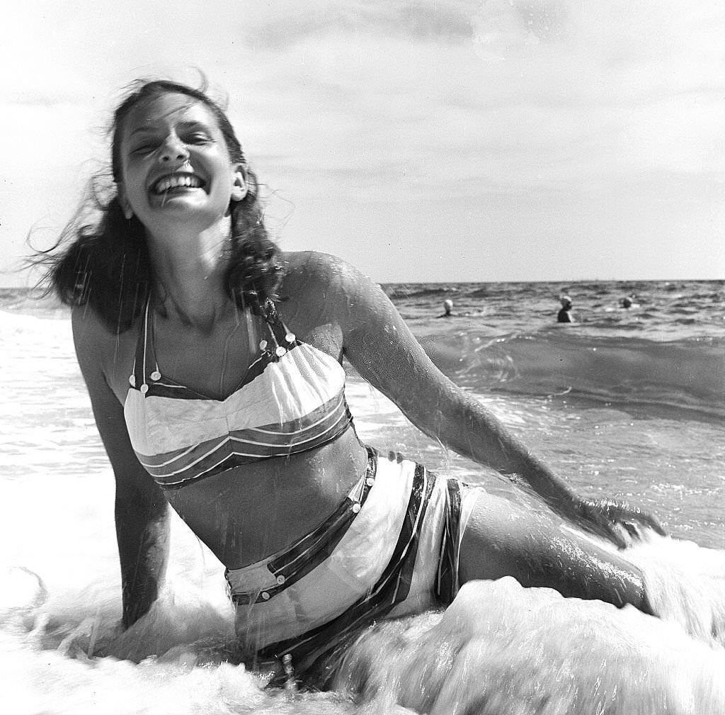 A woman smiles while sitting on the beach as the surf rolls, Provincetown, Massachusetts, 1948.