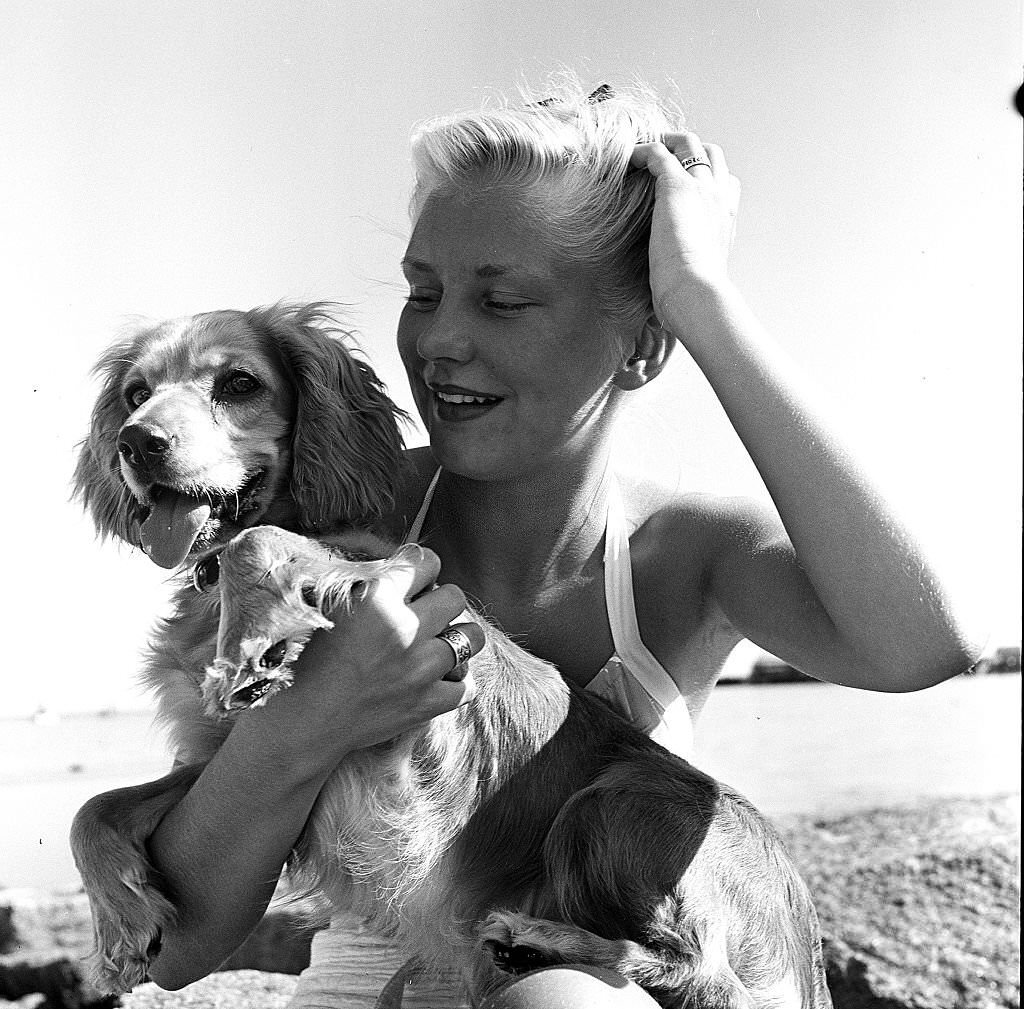 A woman runs her hand through her hair while sitting with her dog, on the beach, Provincetown, Massachusetts, 1948.