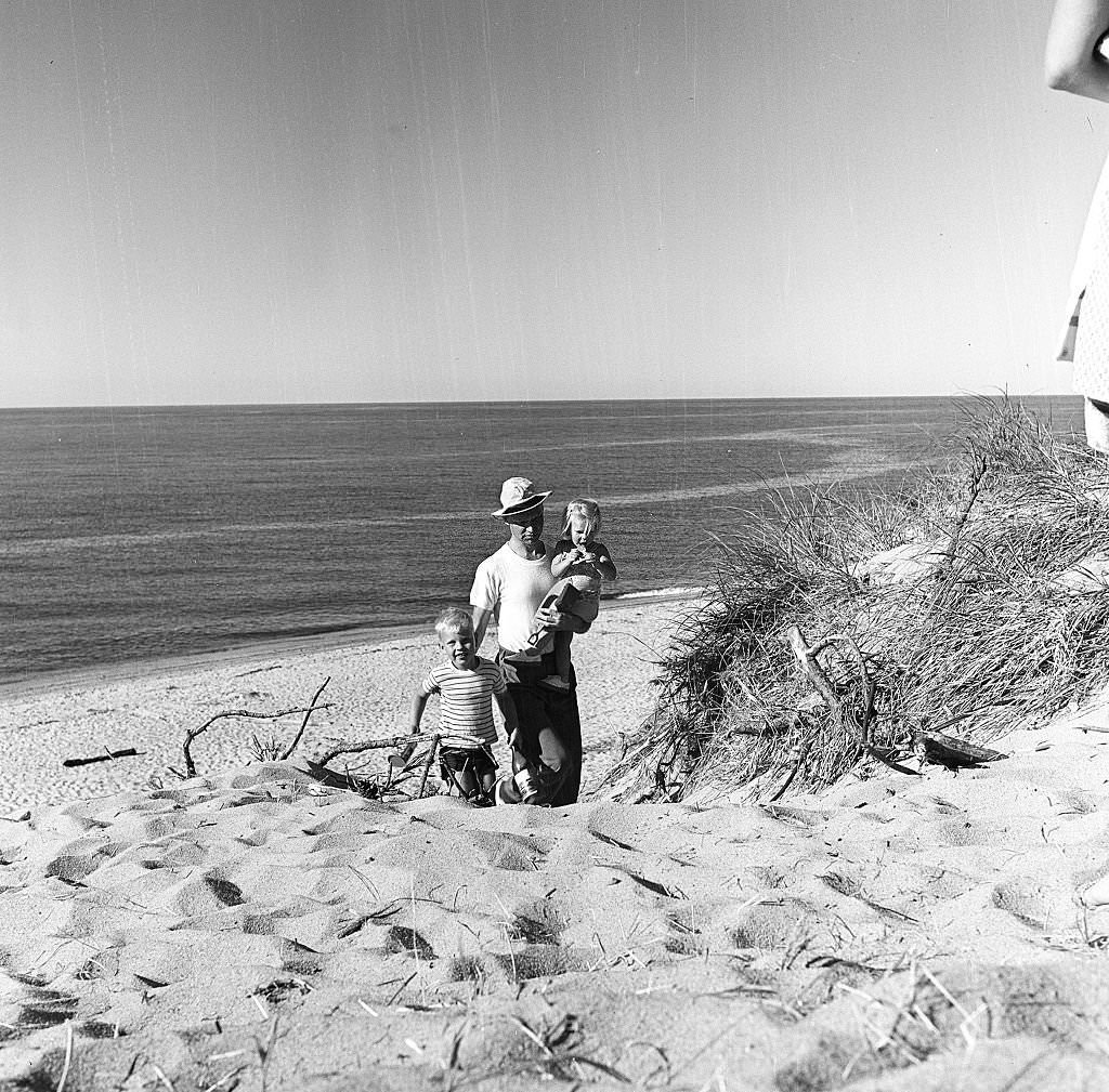 A father carries his daughter and walks alongside his son on the beach, Provincetown, Massachusetts, 1948.