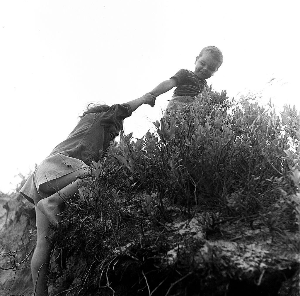 A young boy holds a girl's hand as he helps her up the sand dunes of the beach, Provincetown, Massachusetts, 1948.