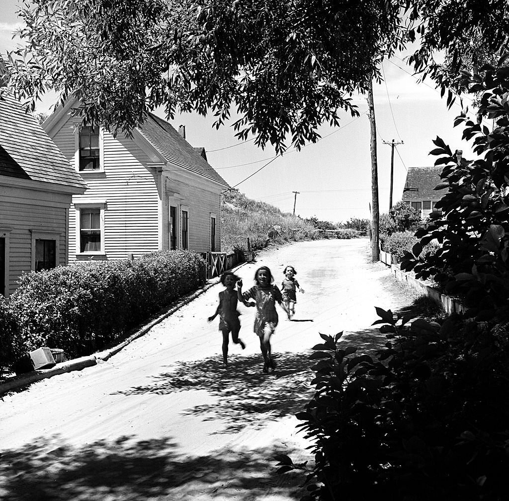 Three children, young girls, smile and run down a street, Provincetown, Massachusetts, 1948.