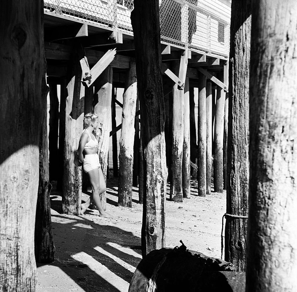 A woman stands amid the wooden pylons of a pier on Cape Cod, Provincetown, Massachussetts, 1947.