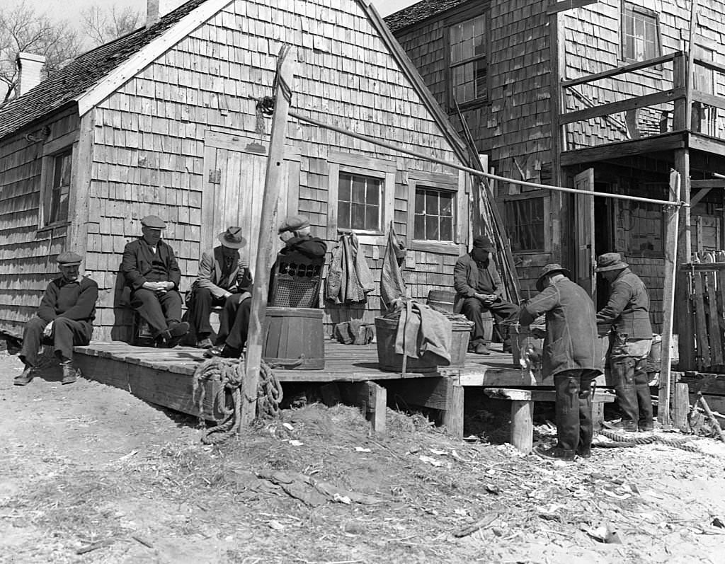 Portuguese dory fishermen sit and talk on the deck of the fishing shack where they store their gear, 1940s