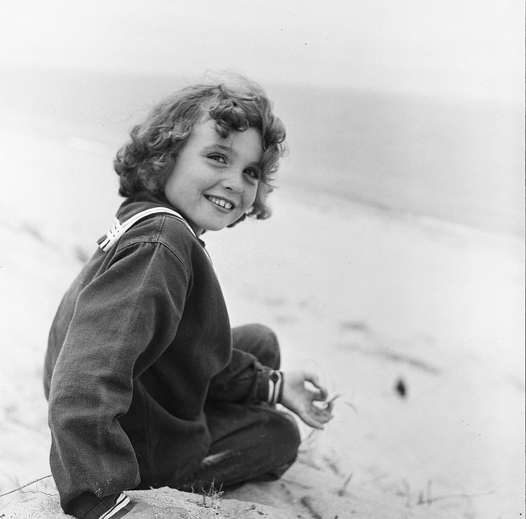 A young girl smiles while sitting on the beach on Cape Cod, Provincetown, Massachussetts, 1947.