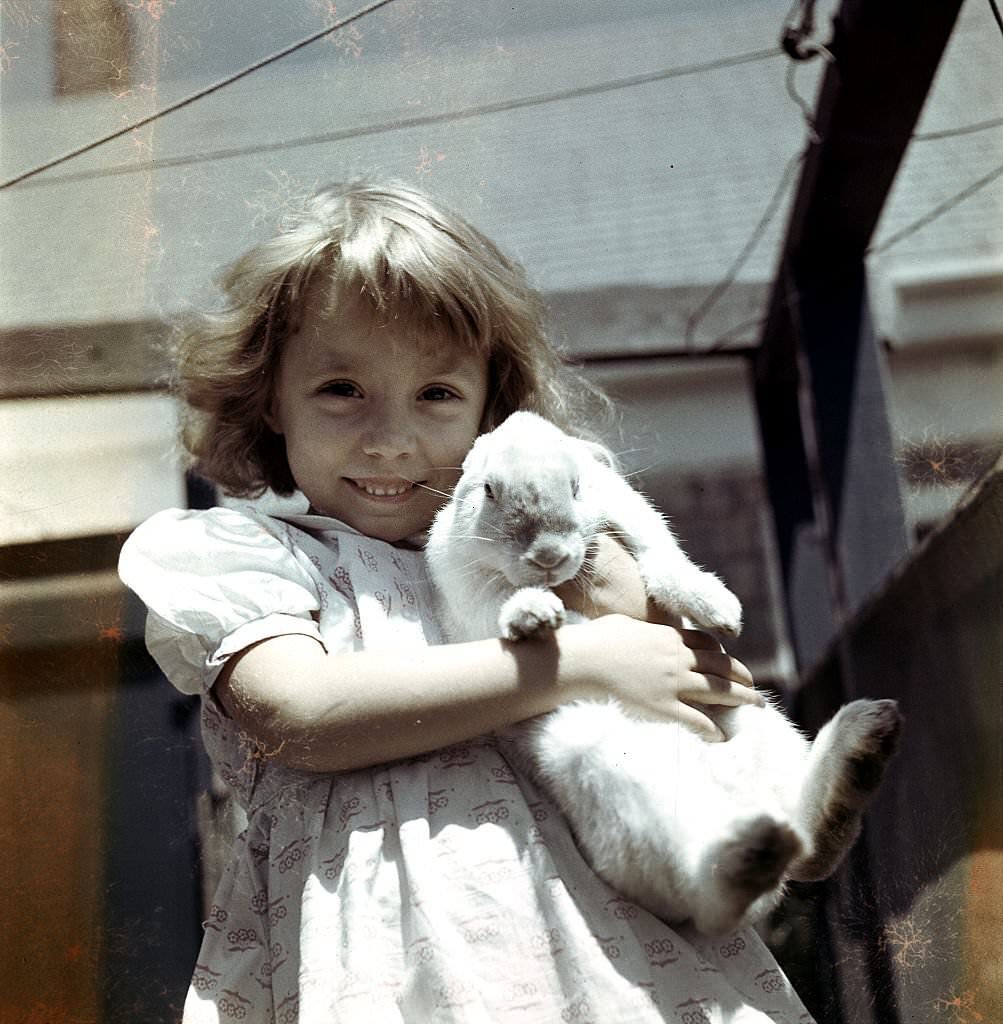 A young girl smiles while holding a white rabbit while visiting, Provincetown, Massachusetts, 1948.