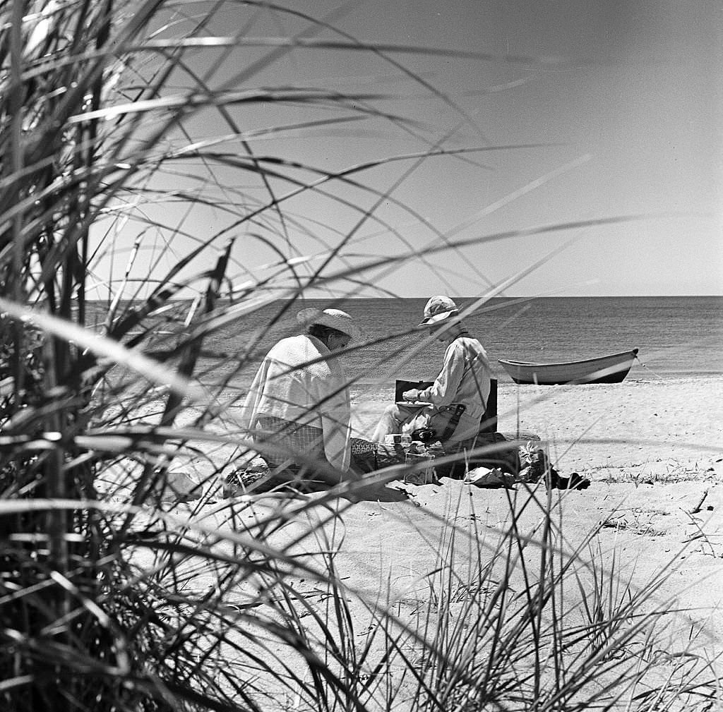 A man and a woman, partially obscured by brush, have a picnic on the beach on Cape Cod, Provincetown, Massachussetts, 1947.