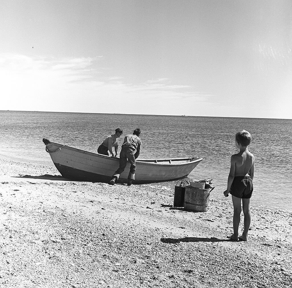 A young boy watches two fishermen head out on a boat on Cape Cod, Provincetown, Massachussetts, 1947.