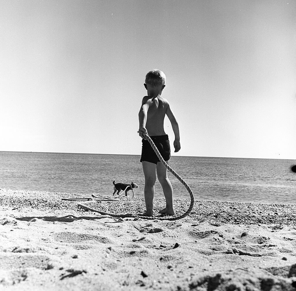 A young boy plays with a rope and his dog on the beach on Cape Cod, Provincetown, Massachussetts, 1947.