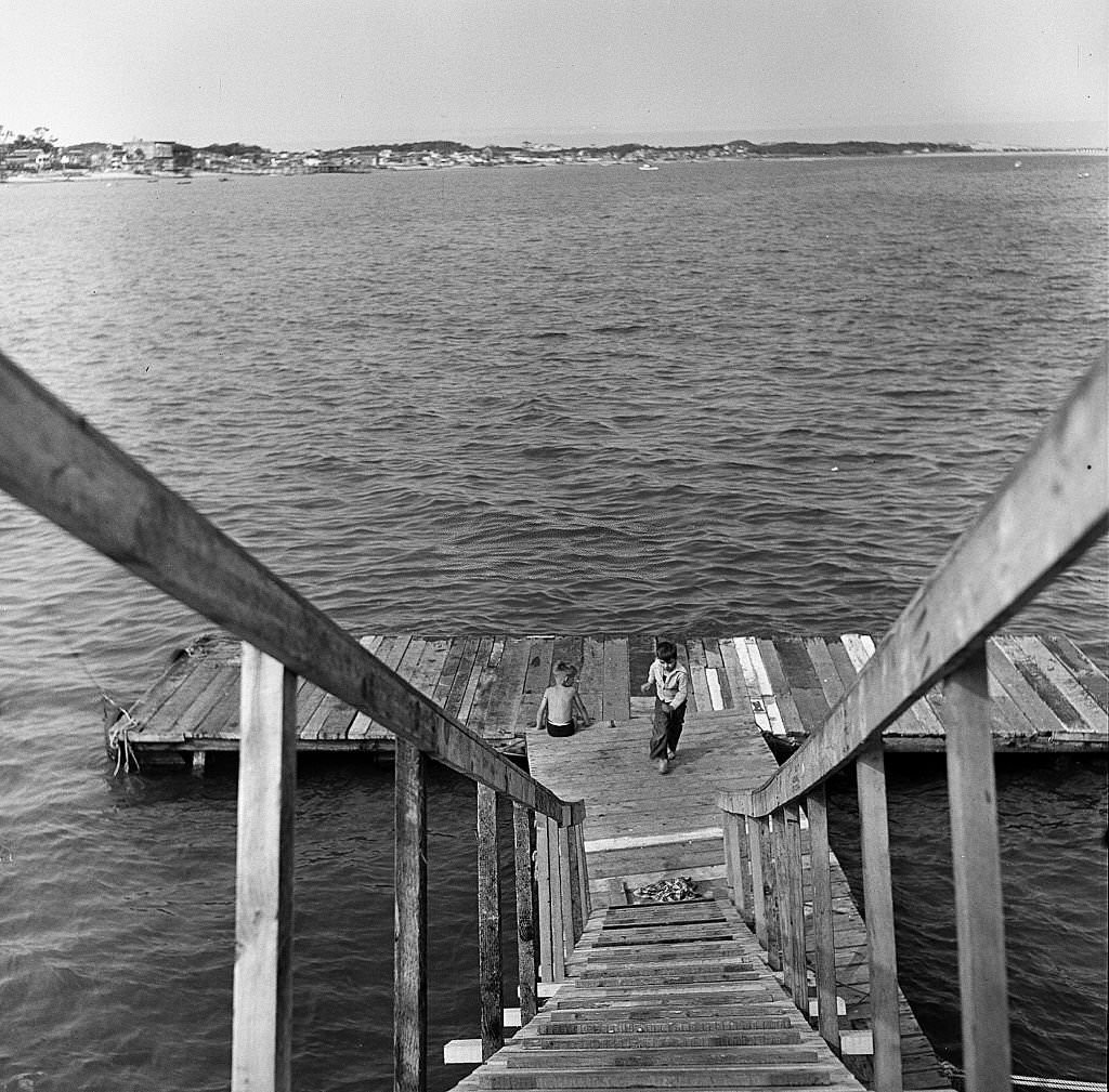 View, looking down stairs, at boys playing at the end of a pier on Cape Cod, Provincetown, Massachussetts, 1947.