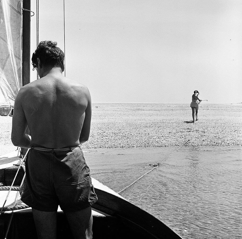 A woman walks ahead to anchor the sailboat on the beach as a man waits to debark on Cape Cod, Provincetown, Massachussetts, 1947.