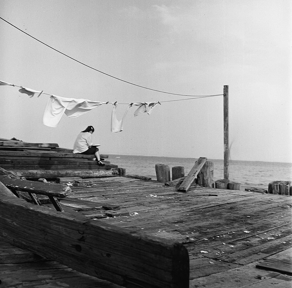 acing the ocean, a girl sketches or writes in her book while sitting on the pier, Provincetown, Massachusetts, 1948.