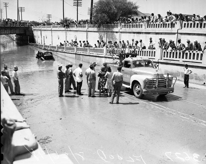 Crowds watch a wrecker pull a car from flooded San Pedro underpass, 1948