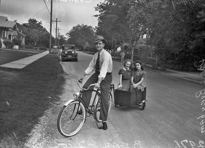 Charles Merritt on bicycle, pulling trailer holding Mary Catherine Grimes and Doris Burnham, 1942