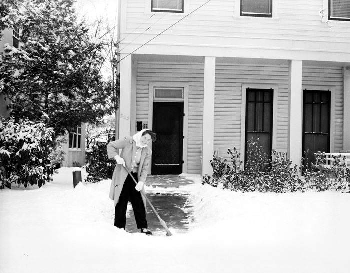 Woman sweeping snow off sidewalk, 1949