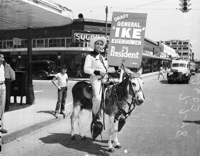 Wally West in western clothing carrying sign, riding donkey, 1948