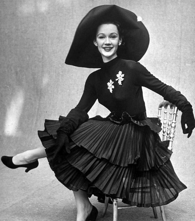 Sophie Malgat in skirt featuring three tiers of pleats worn with long sleeved top and picture hat by Jacques Fath, February 1951