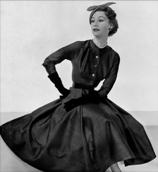 Sophie Malgat is wearing a dark gray alpaca wool dress with ample skirt, buttoned bodice is ruched around the neckline, by Pierre Clarence, 1953
