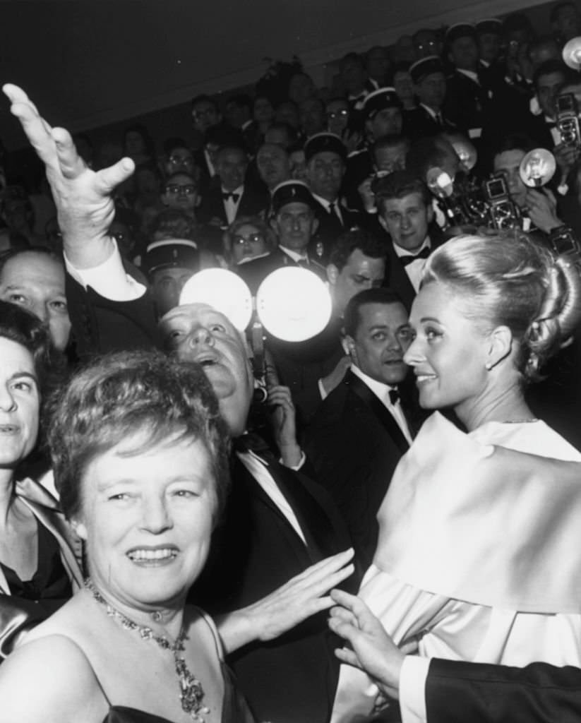 Alfred Hitchcock raising his hand in the air, with actress Tippi Hedren (right) and Mrs Hitchcock (close to camera) at the premiere of the film 'The Birds' at Cannes, May 11th 1963.