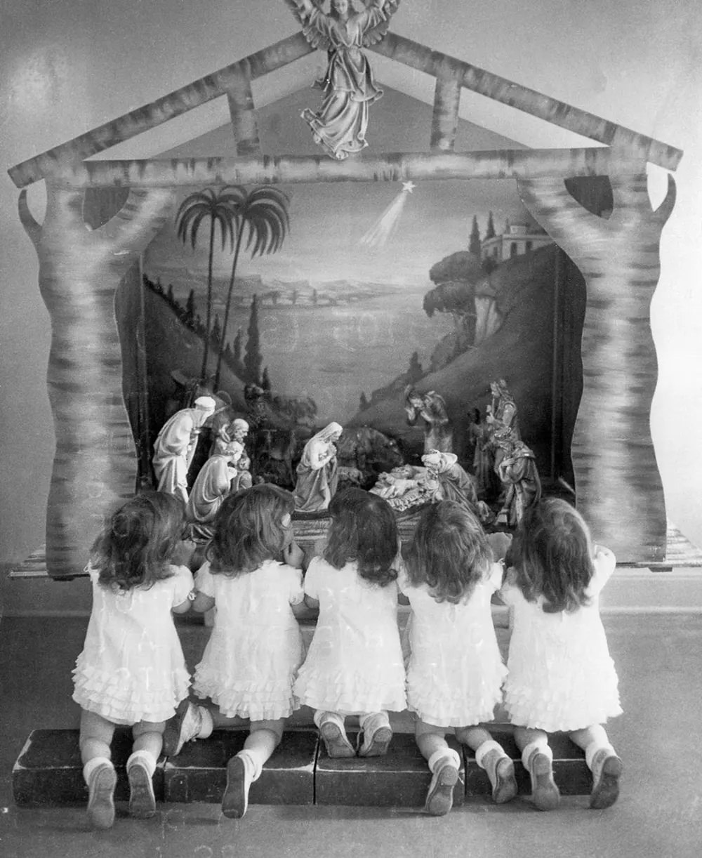 The two-year-old quintuplets kneel before a Christmas creche.