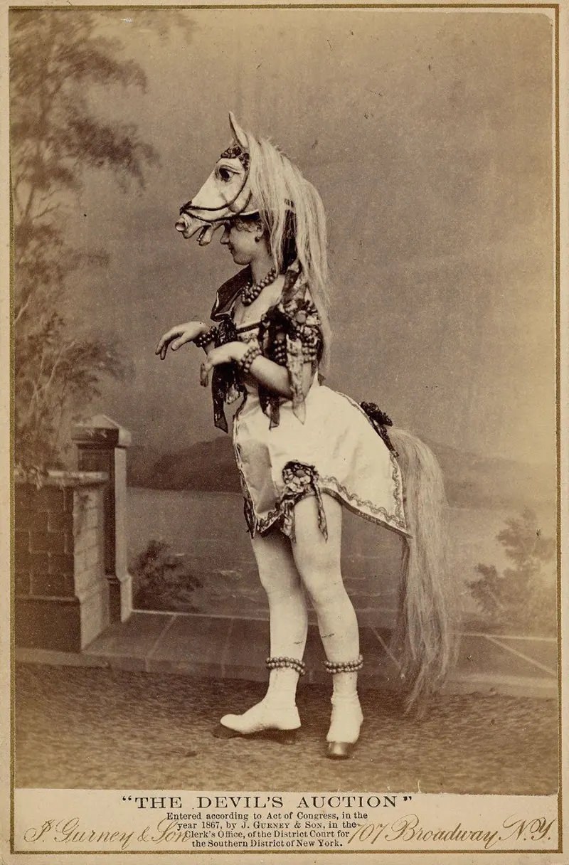 Eliza Blasina wearing horse-head headdress, short costume with attached horsetail, rows of round beads or bells around ankles, wrists, neck and upper arm.