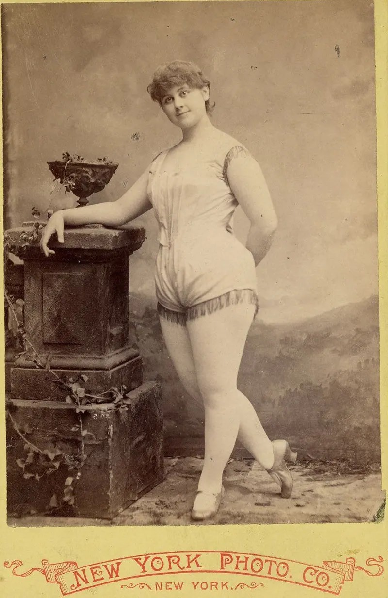 Clara Davenport in a short sleeveless costume fringed at legs and armholes.