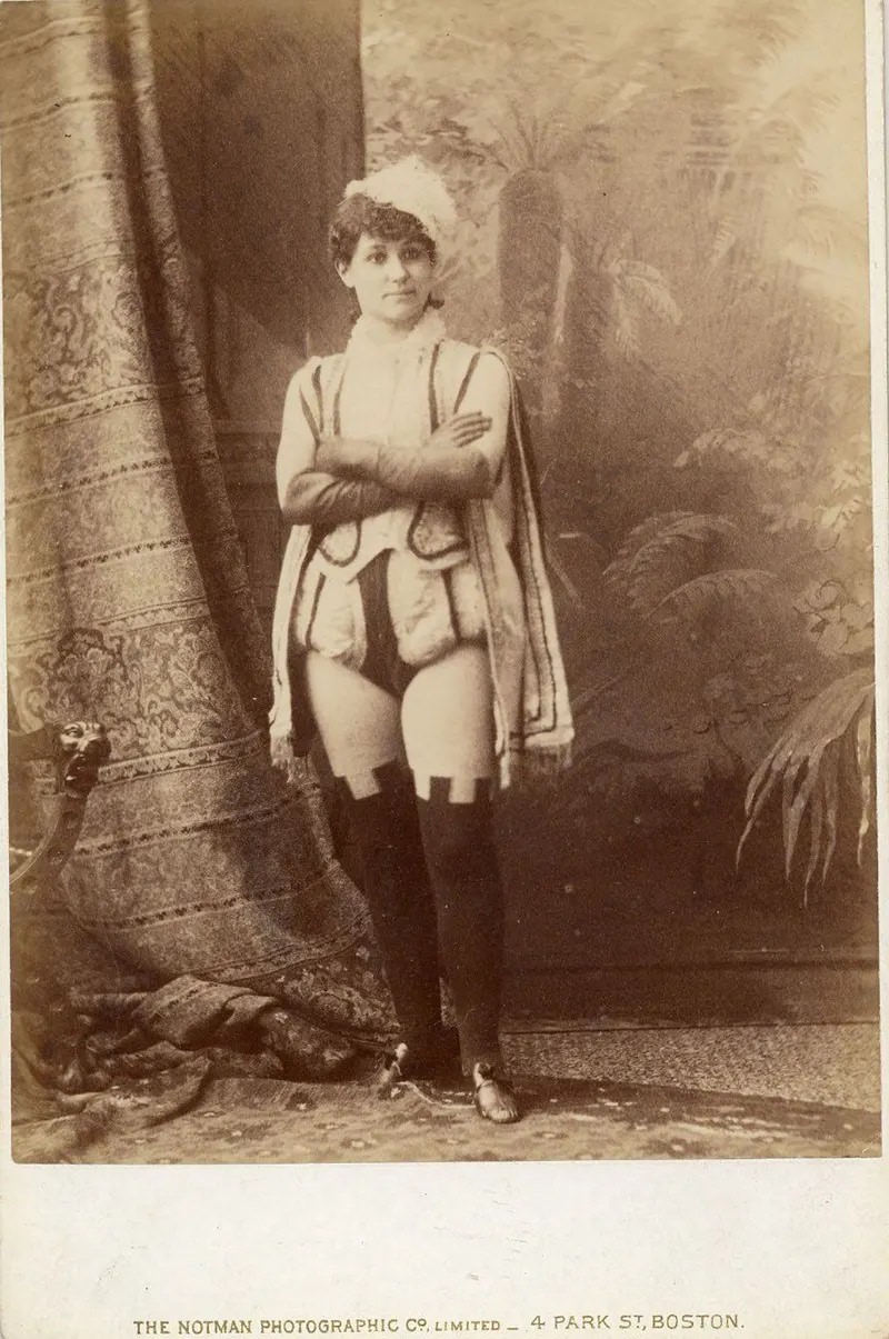 Miss Darcey in short male Renaissance costume with over-the-knee leggings.