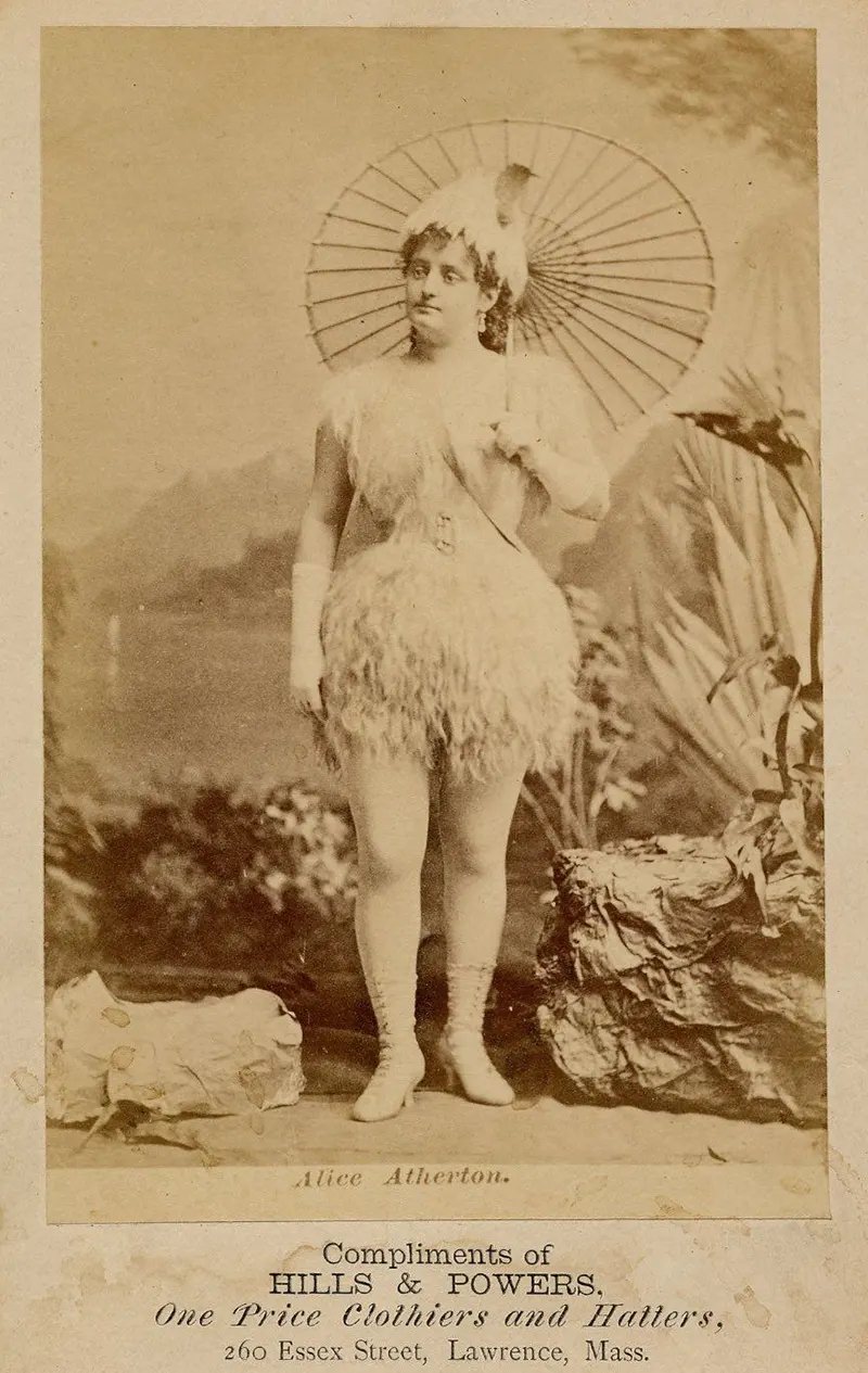 Alice Atherton in a short, feathery costume, tights, parasol, mid-forearm white gloves, mid-calf white heeled and laced boots, feathery hat.