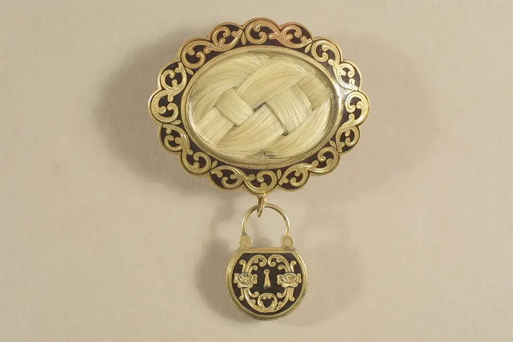 A gold and black mourning brooch with a plait of the deceased’s hair under glass.